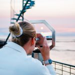 Junge Frau schaut durch ein Fernglas an der Wurster Nordseeküste