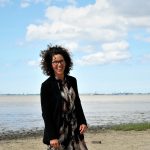 Das Bild zeigt die Moderatorin Carola Schede des NordseeTourismusTags 2026 in Leer. Carola Schede steht am Strand.