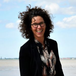 Das Bild zeigt die Moderatorin Carola Schede des NordseeTourismusTags 2026 in Leer. Carola Schede steht am Strand.