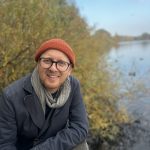 Das Bild zeigt Jonas Løvschall-Wedel an einem See. Er trägt Mütze, Brille und Jacke. Jonas hält einen Vortrag auzf dem NordseeTourismusTag in Leer.