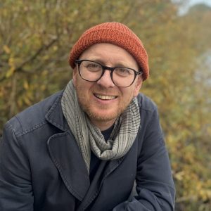 Das Bild zeigt Jonas Løvschall-Wedel an einem See. Er trägt Mütze, Brille und Jacke. Jonas hält einen Vortrag auzf dem NordseeTourismusTag in Leer.