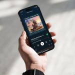 Das Bild zeigt eine linke menschliche Hand die ein Smartphone in der Hand hält. Auf dem Display ist der TANO-Podcast mit der Robbe Fiete zu sehen.