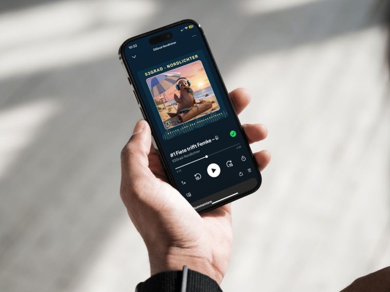 Das Bild zeigt eine linke menschliche Hand die ein Smartphone in der Hand hält. Auf dem Display ist der TANO-Podcast mit der Robbe Fiete zu sehen.
