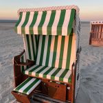 Das Bild zeigt einen geöffneten Strandkorb am Strand von Spiekeroog im roten Abendlicht.