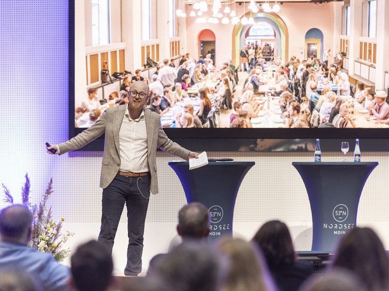 Jonas Løvschall-Wedel, Head of International Communication at Wonderful Copenhagen and Lead of CopenPay, mit ausgebreiterten Armen auf der Bühne vom NordseeTourismusTag in Leer.